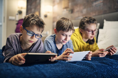 Three kids are lying on bed and playing with modern mobile devices - tablets and smartphone.
Nikon D850