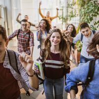 Large group of cheerful students running through school hallway.