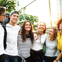 Smiling happy young adult friends arms around shoulder outdoors 