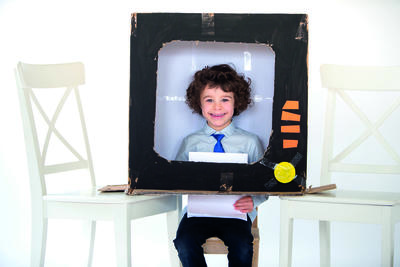 Little boy playing in a cardboard box made to look like a television.