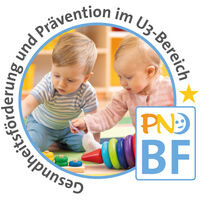 Zwei Kleinkinder sitzen gemeinsam auf dem Boden und spielen mit Holzringen.